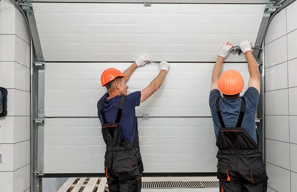 Two workers installing a garage door using tools in a modern garage.