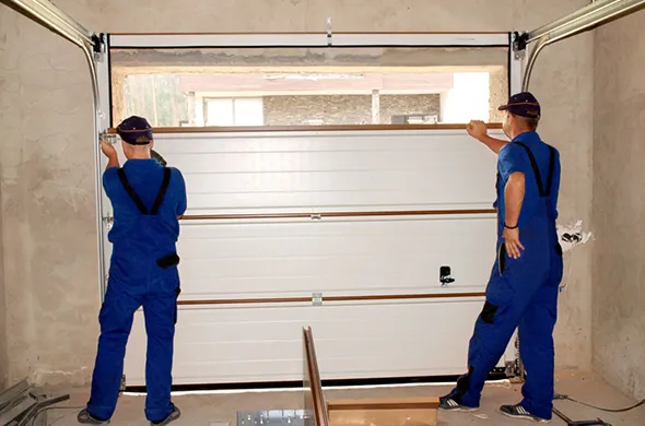 Two garage door contractors putting in a new garage door inside a home.