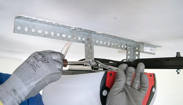 A worker sets up a garage door opener, using tools to adjust parts for safety.