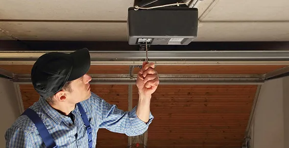 Worker fixing a garage door opener with a tool.