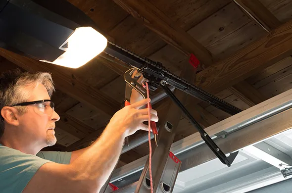 Technician fixing a garage door opener under a light in a workshop.