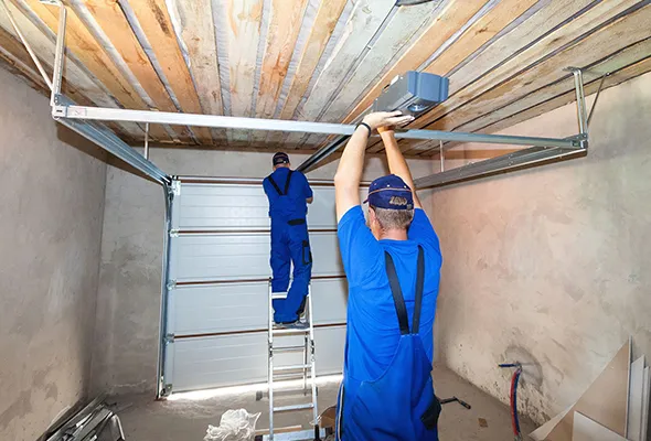 Two workers are installing a garage door system using a ladder in a bright garage.