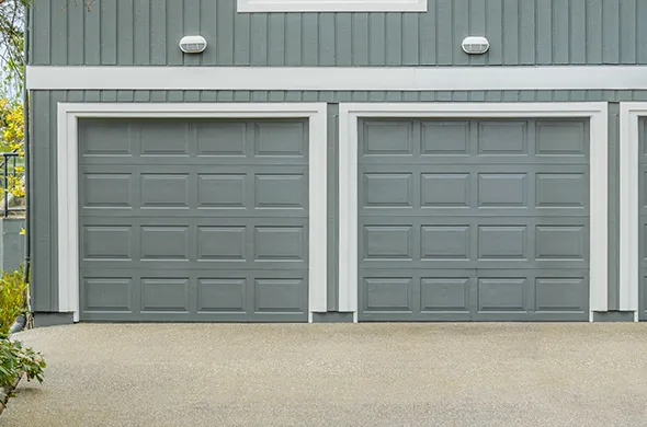 Stylish custom garage door installation with two gray doors on a house driveway.